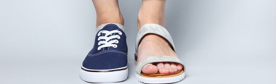 Frauenfüße in einem Sneaker und einer Sandale